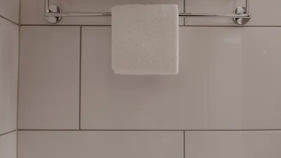 Pyyhetelineellä on taiteltuja valkoisia pyyhkeitä; lasi on ylösalaisin laatoitetulla tasolla alla. Seinälaatat muodostavat minimalistisen kylpyhuoneympäristön.