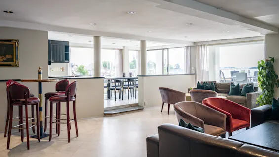 Et romslig og innbydende hotelloungeområde med ulike sittegrupper, inkludert en bar og komfortable sofaer, med utsikt.