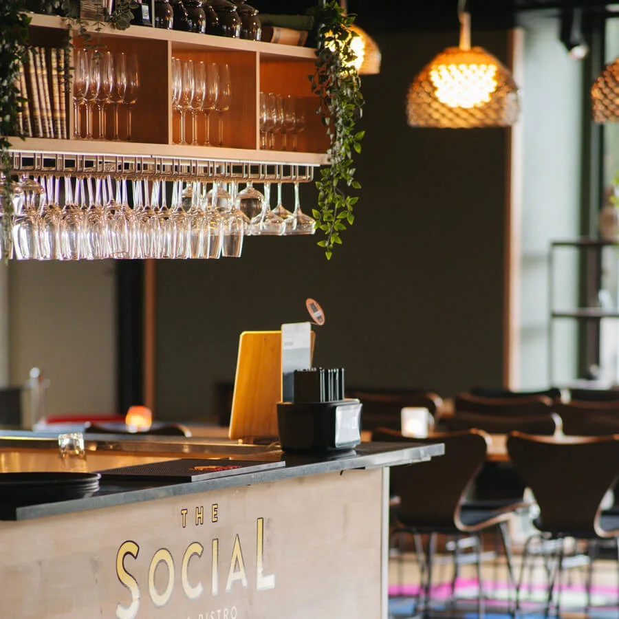 Bardisk dekorerad med glas och gröna växter, placerad i en stilfull bistro med flätade lampor och moderna sittplatser. Text på disken: "THE SOCIAL BAR & BISTRO"