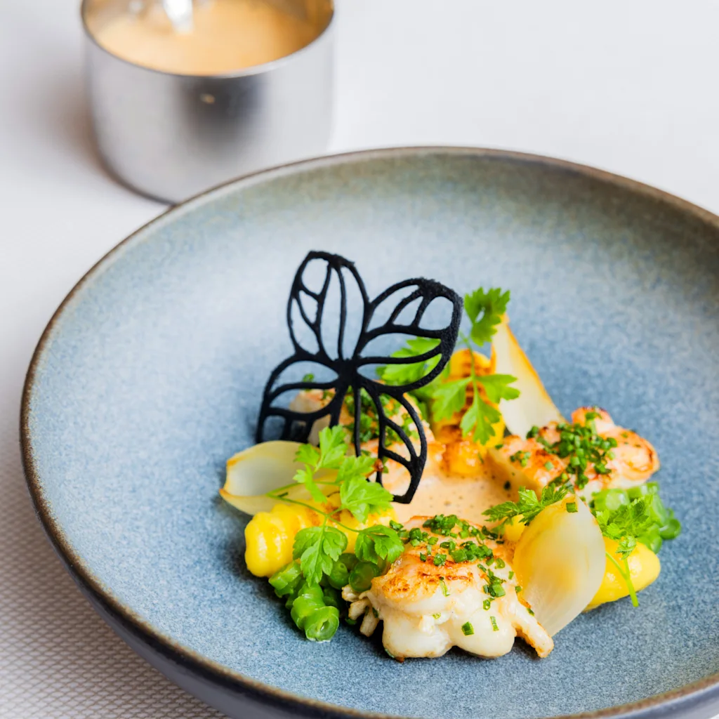 Et smukt anrettet måltid med skaldyr, gule grøntsager og grønne urter, pyntet med en dekorativ sommerfugl.