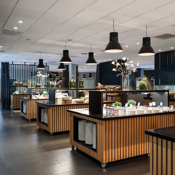 Buffetbordene viser forskjellige retter i et elegant, moderne spiserom. Taklysene belyser de pent arrangerte rettene, og skaper en innbydende atmosfære med stilrene svarte og trefargede detaljer.