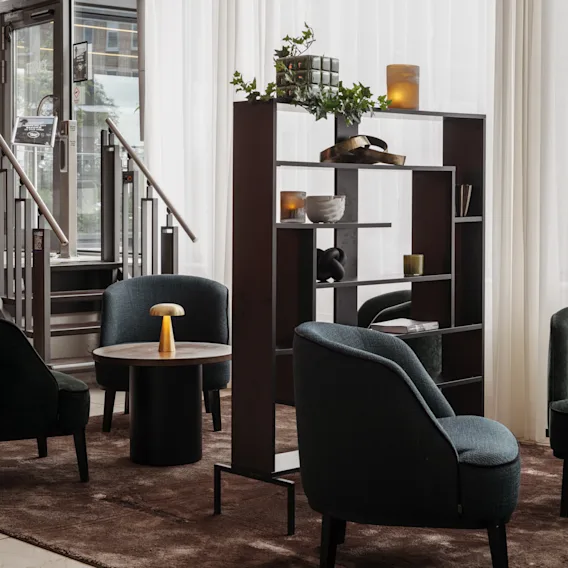 En mysig hotellounge med mörka fåtöljer, en bokhylla med inredning och en trappa som leder upp. 