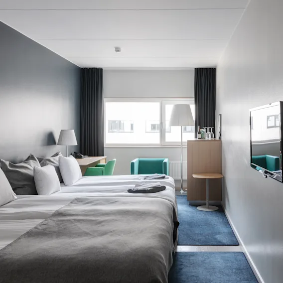 Modern hotel room with multiple single beds lined up next to each other, a wall-mounted TV, and a window.