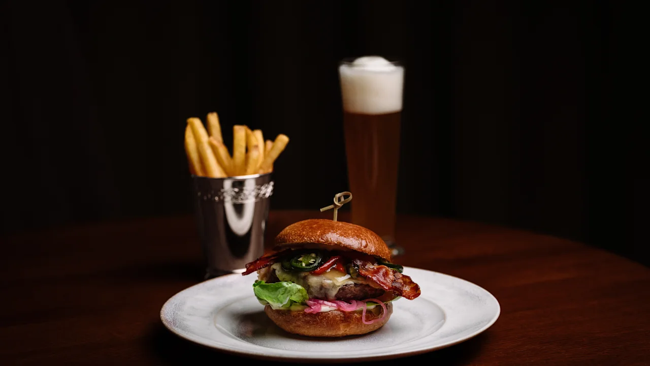 Herkullinen hampurilainen ranskalaisten ja oluen kera puupöydällä Hotel Kämp – Ravintola A La Kampissa.