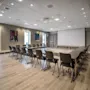 A modern conference room with a U-shaped table setup, chairs, a large projection screen, and windows, ready for a meeting.