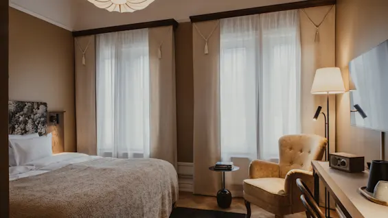 Home Hotel Baltzar - Standard Twin. A cozy room with a comfortable bed, armchair, and desk, bathed in soft natural light.