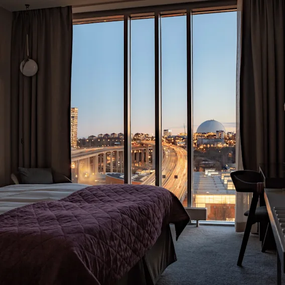 Ett hotellrum med ett stort fönster som visar en skymningsvy över en motorväg i staden och en stor, upplyst sfärisk byggnad i fjärran.