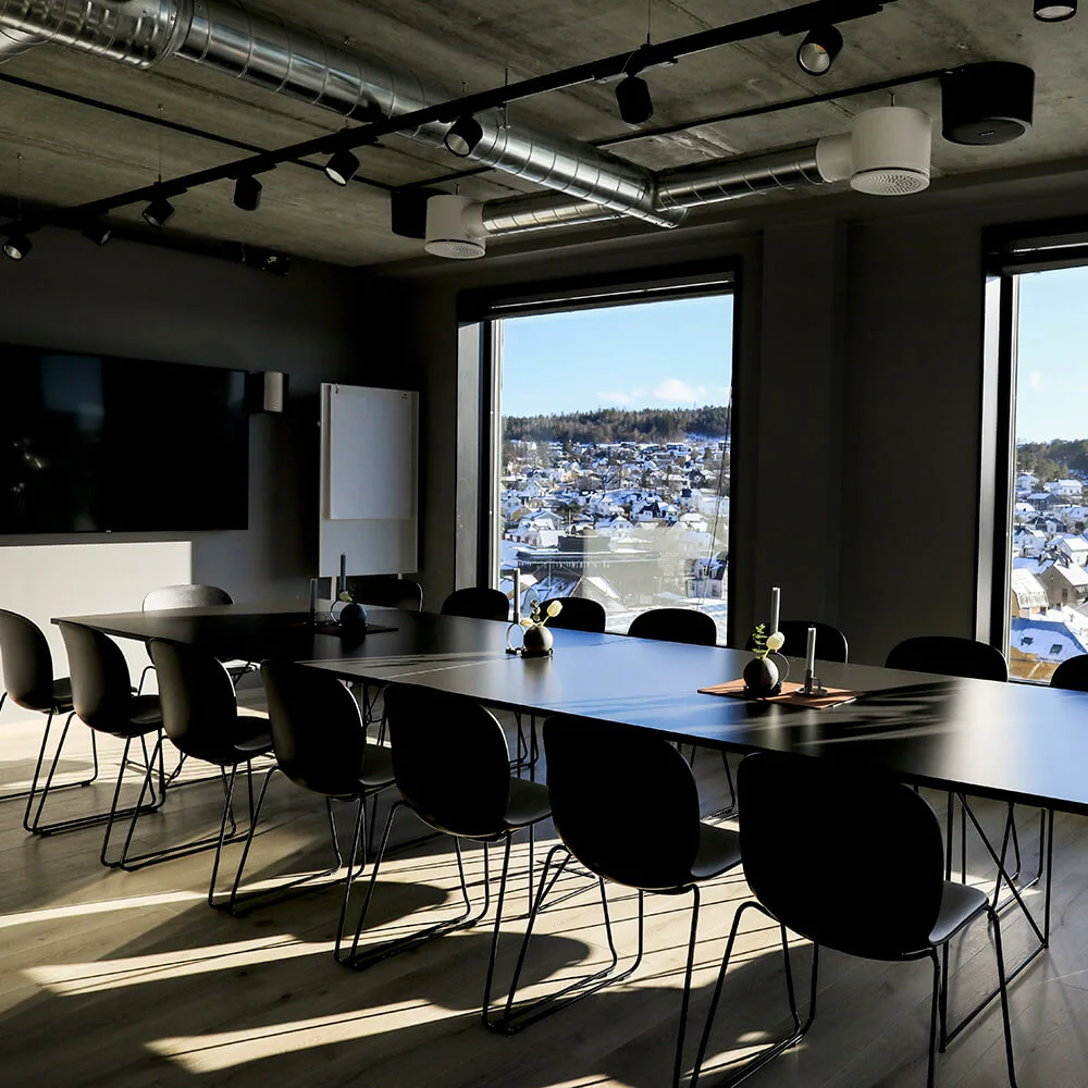 Et moderne konferencerum med et langt bord omkranset af stole, store vinduer, der viser en sneklædt by. Indendørs planter og et synligt whiteboard bidrager til det professionelle miljø.