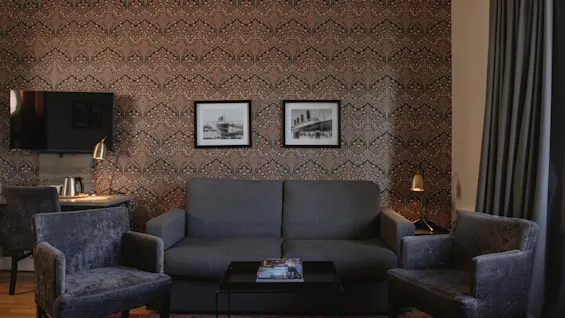 Ett mysigt hotellrum med en bekväm sittgrupp, ett skrivbord och dekorativ mönstrad tapet, perfekt för avkoppling.