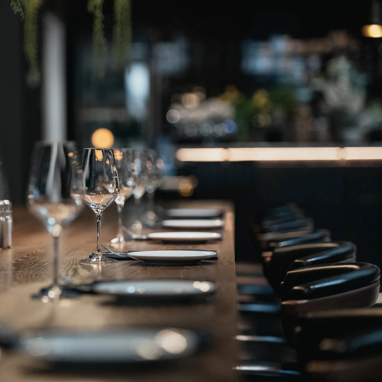 Elegantly set dining table with place settings and glasses, ready for guests in a dimly lit, sophisticated restaurant.