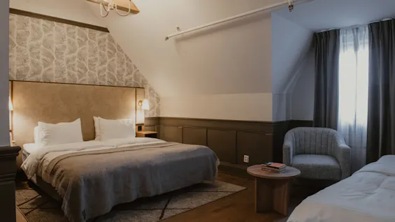 Et elegant hotelværelse med stor seng, mønstret væg og komfortabel lænestol ved vinduet.