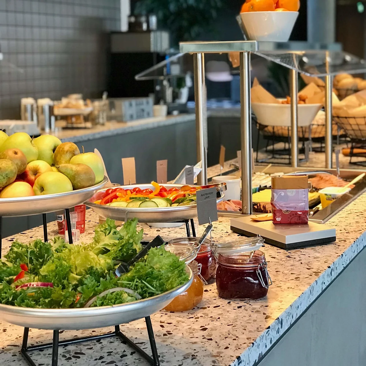 Et buffetbord viser frugt, grøntsager og krydderier i et moderne spiseområde med blød belysning og grønne omgivelser.