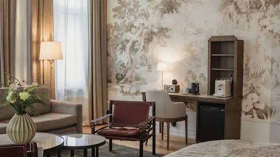 Home Hotel Baltzar - Junior Suite. A cozy hotel room with a sofa, desk area, and nature-themed wallpaper.