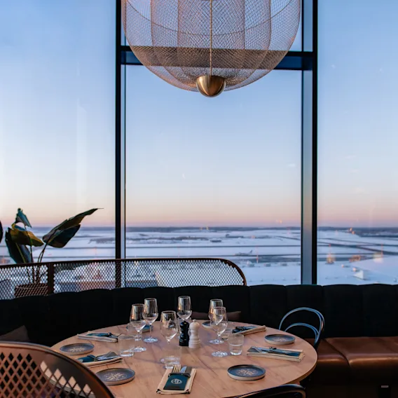 En moderne restaurant med dekket bord og store vinduer med utsikt over et snødekt landskap i skumringen.
