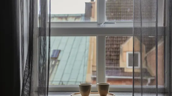 Mysig fönsterutsikt från Home Hotel Grand, Helsingborg, med två koppar på fönsterbrädan och takåsar utanför.