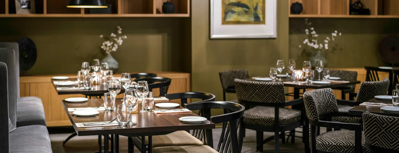 En hyggelig moderne restaurant med flot opdækkede borde, blød belysning og elegant indretning. Varme træfarver og stilfulde møbler skaber en indbydende stemning til en dejlig middag.