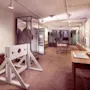 A historical museum exhibit in a long hallway with a wooden stockade, display cases, and framed documents on the wall. Visible text: BRITTISK STRAFF.
