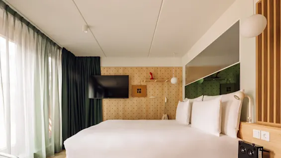 A modern hotel room at Hobo Oslo with a comfortable bed, a TV on a pegboard wall with a HO BO sign, and stylish decor.