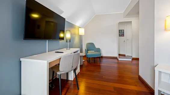 A modern room with a flat-screen TV, desk, chair, and accent armchair, illuminated by soft lighting.