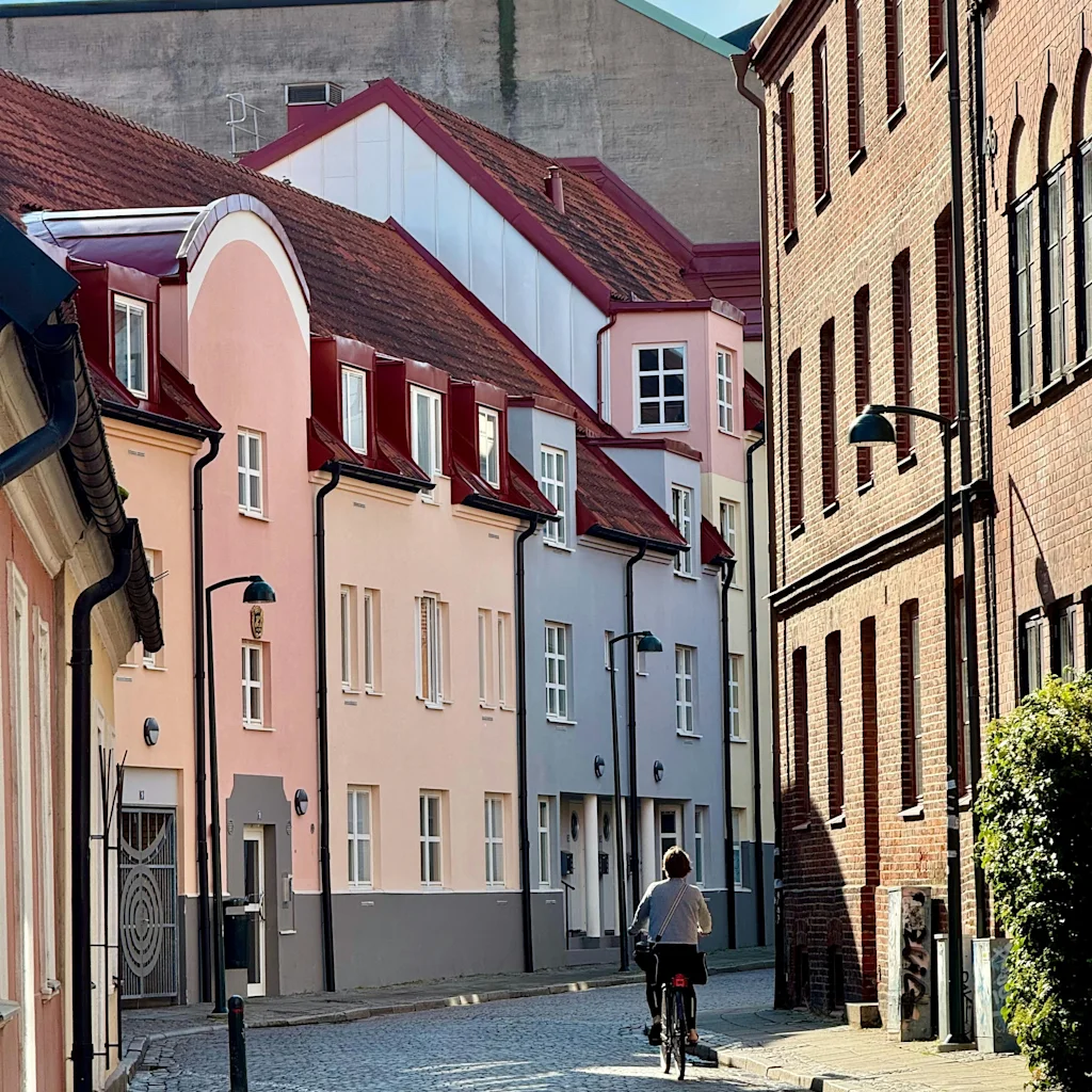 Person sykler på brosteinsgate med fargerike bygninger i Lund. Solfylt dag.