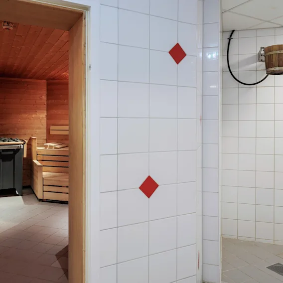 En trebadstue med benker og en ovn til venstre. Et flislagt rom med en trevannbøtte hengende fra veggen til høyre.
