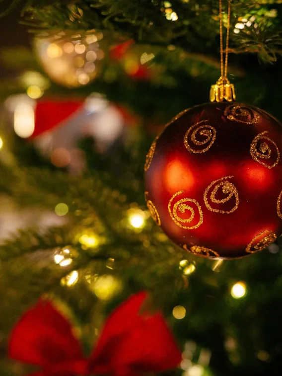 Nærbilde av en rød julekule med gullspiraler på et belyst juletre.