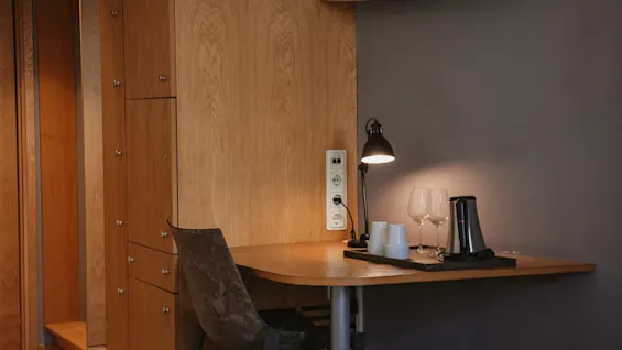 Viihtyisä työpöytäalue hotellihuoneessa lampun, lasien ja vedenkeittimen kera, täydellinen rentouttavaan iltaan Home Hotel Uppsalassa.