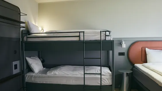 Ett modernt hotellrum på Stopover Hotel Falkenberg med en mörk våningssäng och en intilliggande enkelsäng, redo för gäster.
