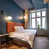Ett modernt hotellrum med dubbelsäng, blå väggar, trägolv och ett stort fönster som släpper in naturligt ljus.