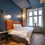 A modern hotel room with a double bed, blue walls, wooden floors, and a large window letting in natural light.