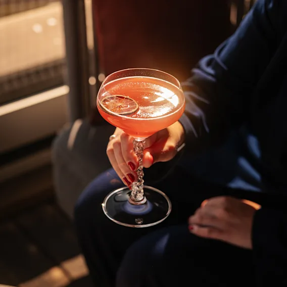 En person håller en livlig cocktail med citrusgarnering på baren på Clarion Hotel Sign.