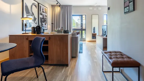 A modern, well-lit room with wooden furniture and herringbone flooring. A dining chair, table, bench, and decorative items create a cozy interior.