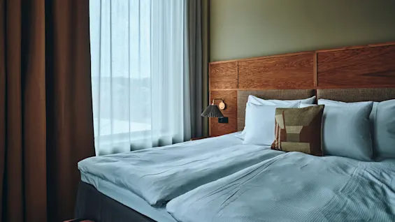 Et koselig hotellrom med en pent oppredd seng, sengegavl i tre og myk belysning, som inviterer til et avslappende opphold.