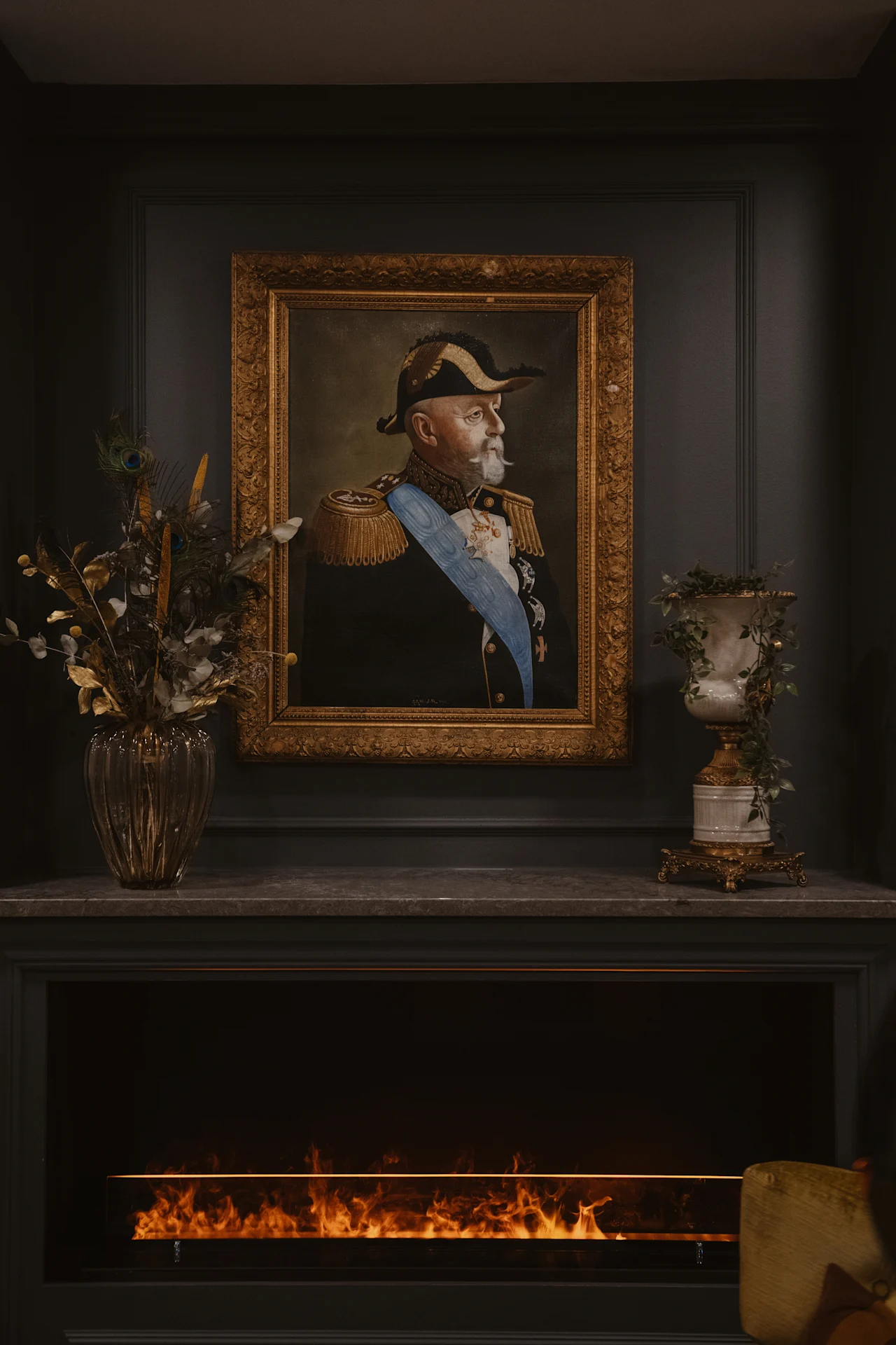 Home Hotel Kung Oscar features a grand portrait of a distinguished figure above a cozy fireplace, flanked by elegant decor.