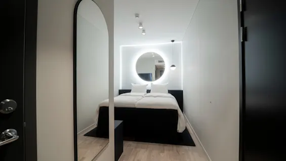 Et moderne, minimalistisk hotellrom på Quality Hotel Strawberry Arena med en seng, sirkulært bakgrunnsbelyst speil og lyst tregulv.