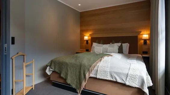 Ett mysigt hotellrum med en stor säng, träpanel och varm belysning. En klädställning syns till vänster.