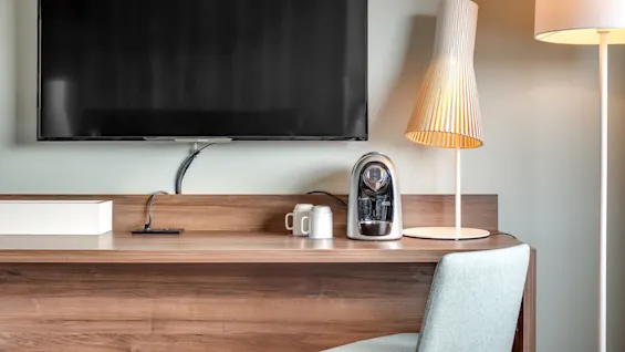 Flat-screen TV mounted on wall above wooden console with lamp, coffee cups and coffee machine; modern, cozy interior feeling.