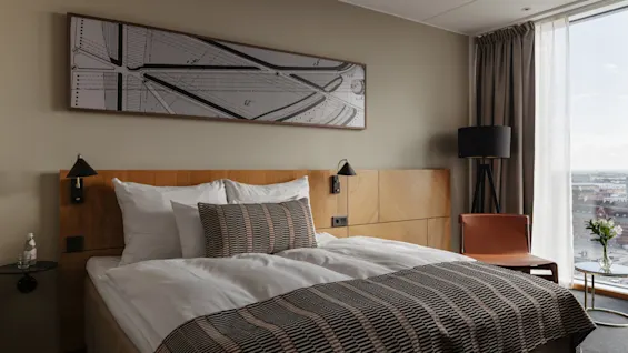 Et moderne hotellrom med en komfortabel seng, et stort vindu med utsikt over byen og moderne innredning.