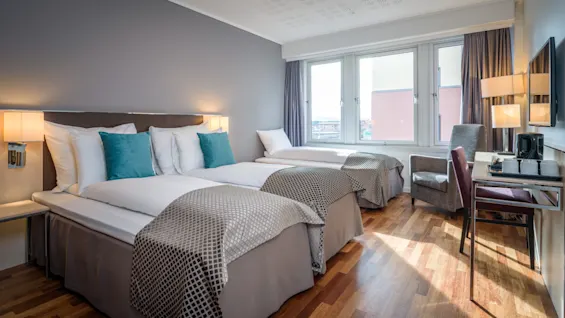 Et komfortabelt hotellrom med to senger, et skrivebord og et stort vindu, som tilbyr et lyst og innbydende rom.