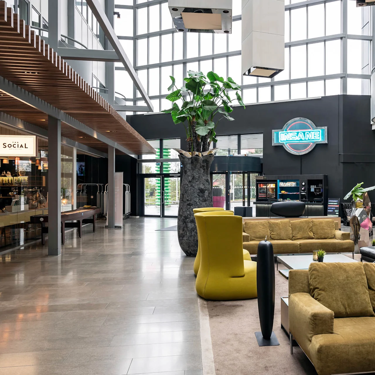Gule sofaer står i en romslig lobby med store vinduer. Neonskiltet "INSANE" på veggen, og kaféen "SOCIAL" til venstre. Moderne og luftig miljø.