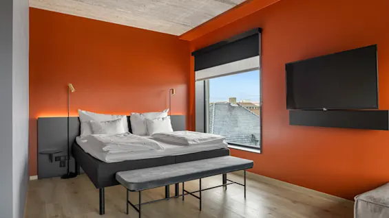 Et stilfullt rom på Comfort Hotel Porsgrunn med oransje vegg, koselig seng, stort vindu og veggmontert TV.