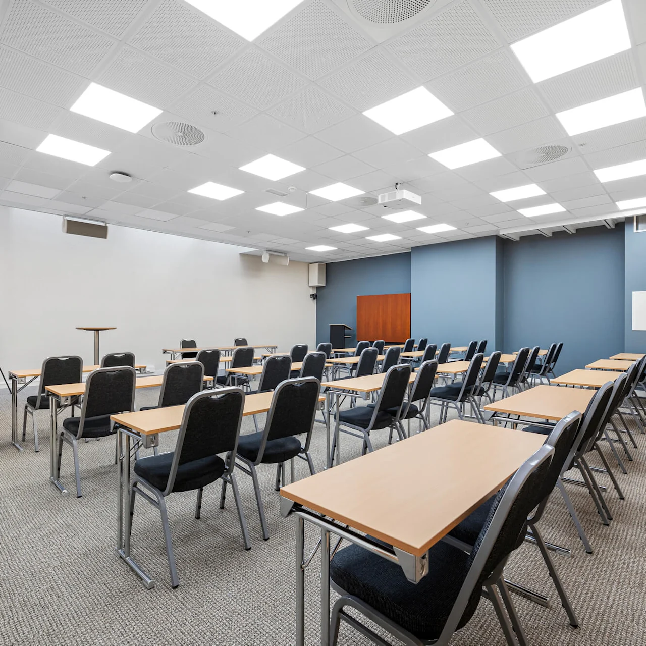 Empty conference room with rows of tables and chairs, clean and organized, with a whiteboard and projector on the walls.
