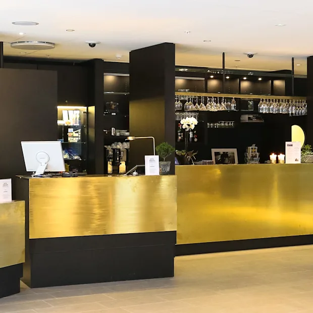 Hotellin vastaanotto- ja baarialue Quality Hotel Oresundissa, jossa on kultaiset tiskit ja henkilö työskentelee vastaanotossa.