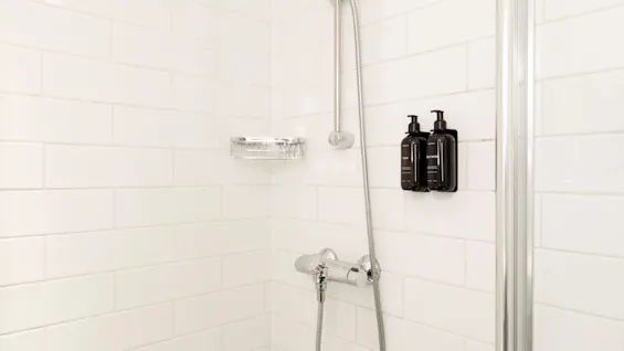 A bright and modern shower area at Home Hotel Grand Bodø, featuring white subway tiles, a shower head, and convenient wall-mounted toiletries.