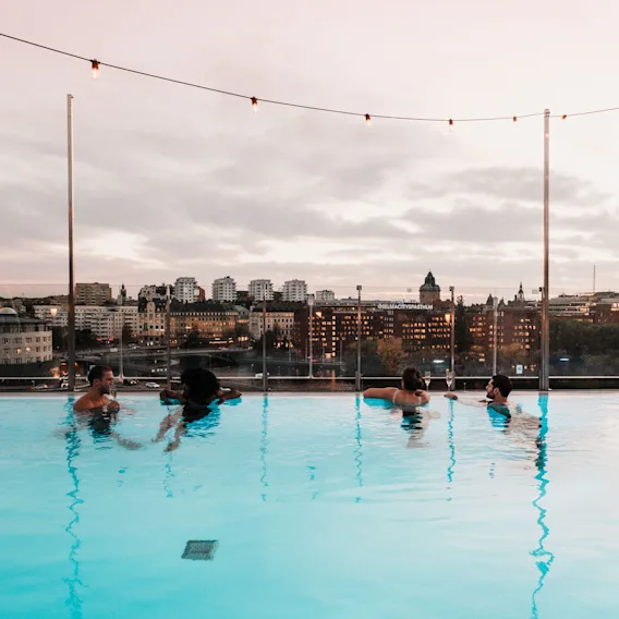 People relaxing in a rooftop pool at Selma City Spa at Clarion Hotel Sign, with a city skyline view at dusk.