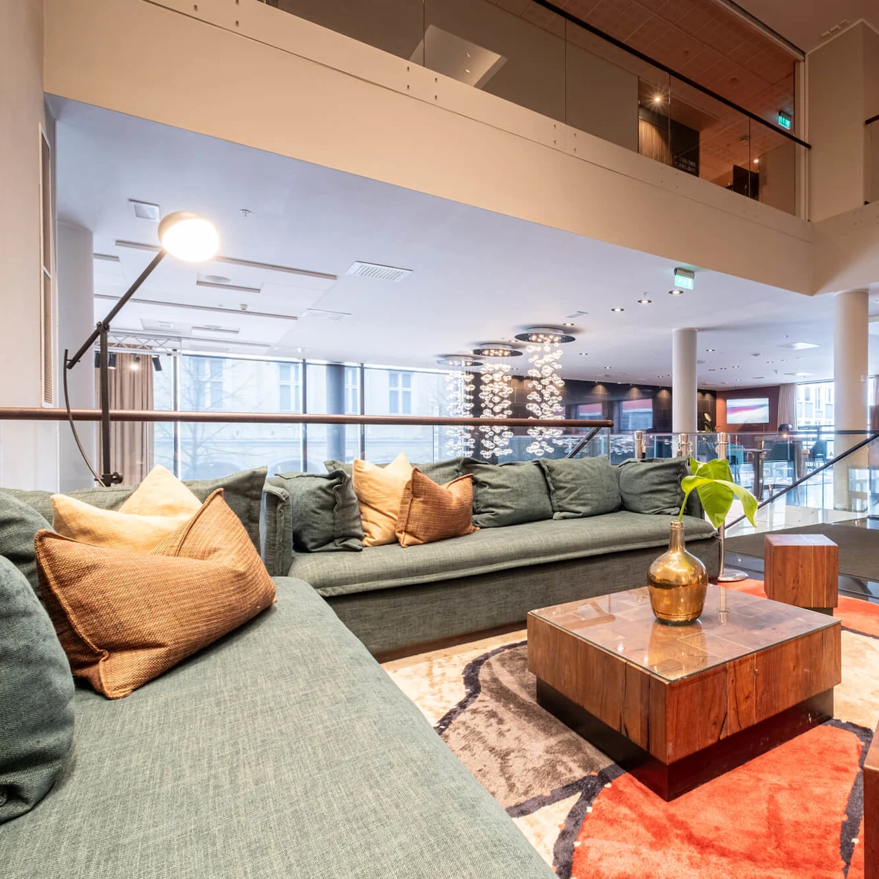 Sophisticated lounge area with a green sectional sofa adorned with tan cushions, centered around a wooden coffee table on a colorful abstract rug, surrounded by modern decor and soft lighting.