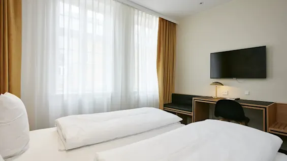Et lyst hotelværelse med to komfortable senge, et funktionelt arbejdsområde og et fjernsyn til underholdning.