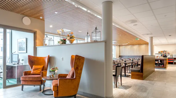Two comfortable chairs sit in a modern, spacious dining area with tables, soft lighting overhead, and a buffet section in the background.