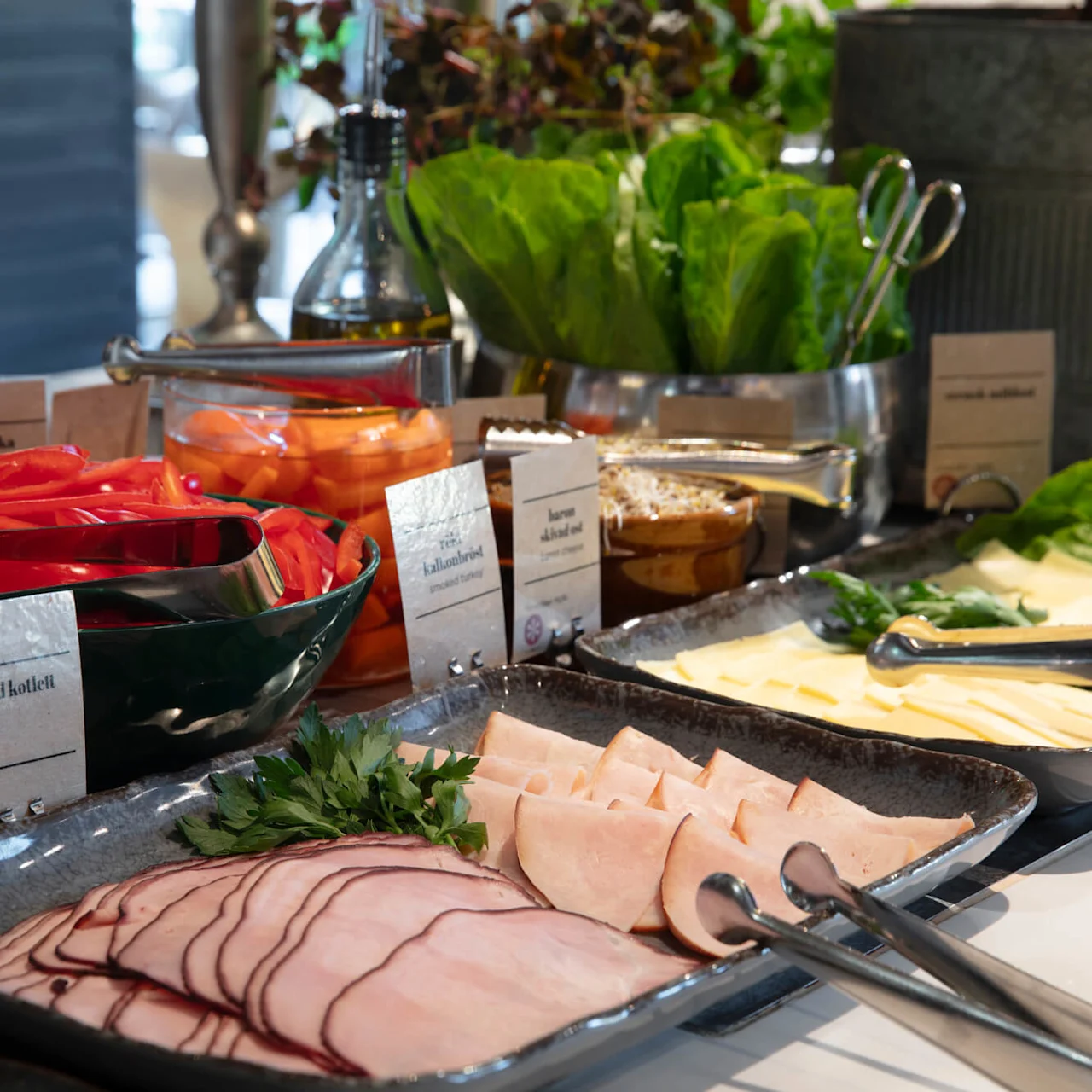 A buffet spread with meats, cheeses, and vegetables, labeled for a selection housed in a modern setting.