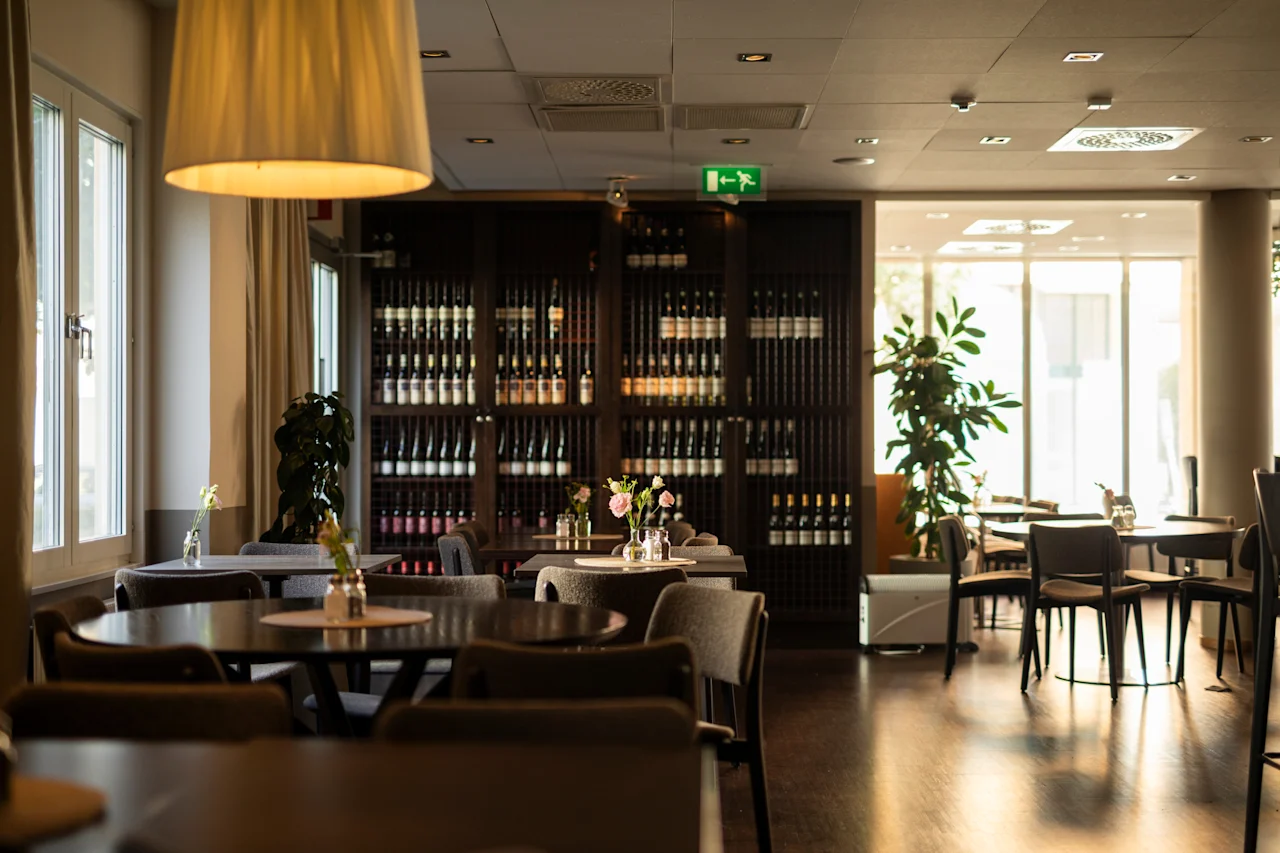 En välkomnande hotellmatsal på Home Hotel Tapto, med bord, stolar, en vinförvaring och ljust naturligt ljus. EXIT.